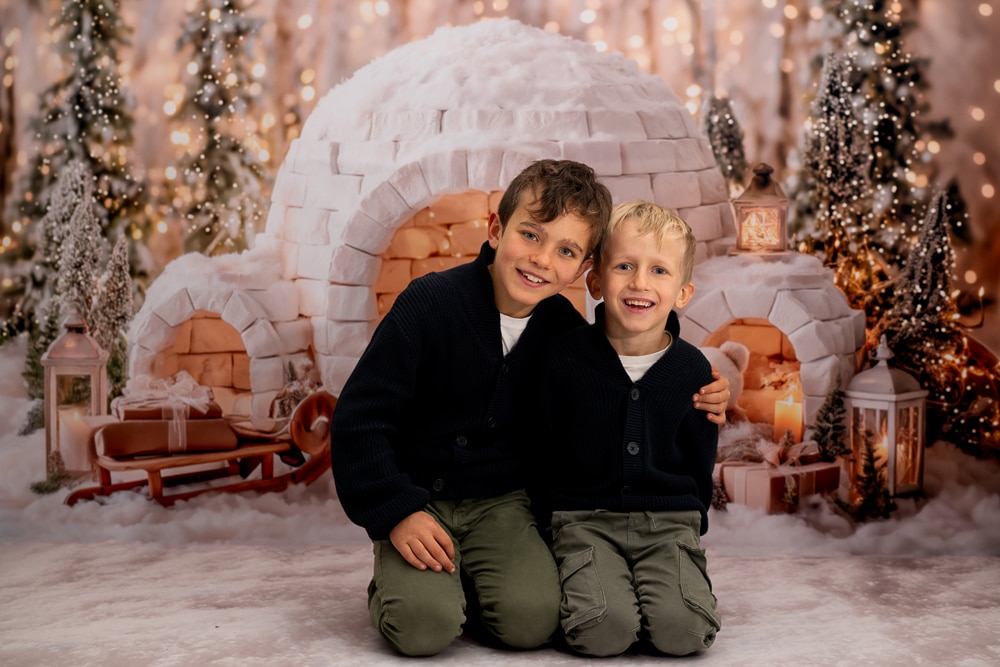 Portrait de frères dans un décor de Noel enneigé-séance photo à Morillon deux frères souriants posent devant un igloo et des sapins illuminés dans un décor de Noel enneigé