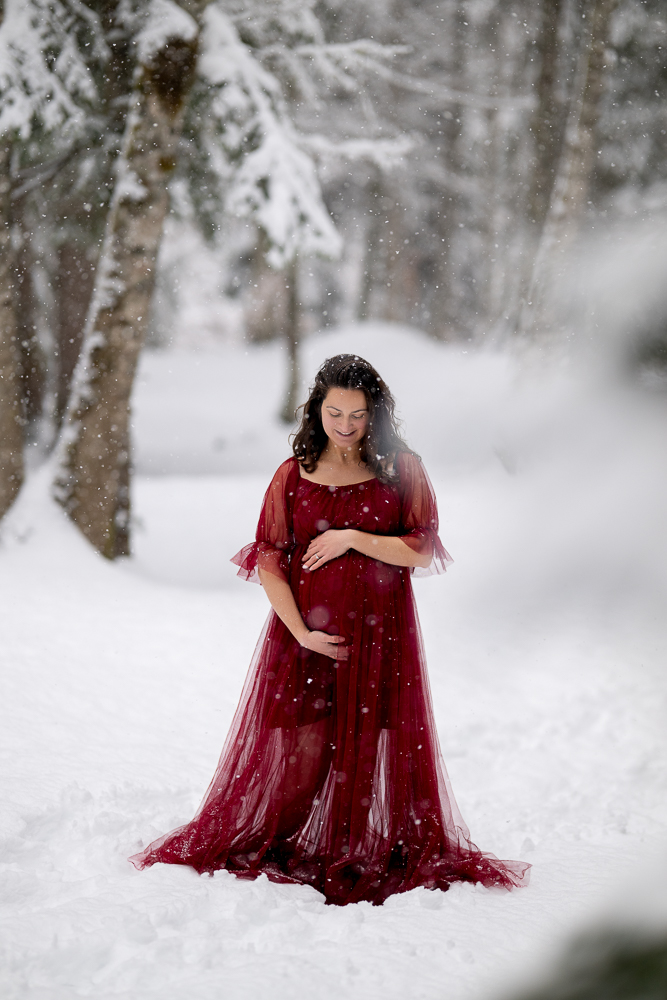 Séance photo grossesse en hiver en Haute-Savoie femme enceinte en robe rouge dans la neige à Samoëns