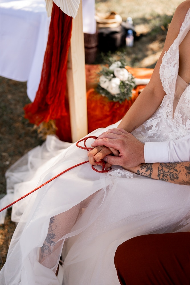 Instant d’émotion pendant une cérémonie de mariage-6 Les mains des mariés s’entremêlent lors d’un rituel de cérémonie laïque en Haute-Savoie, photographié par une photographe de mariage à Samoëns.